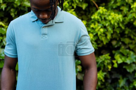 Téléchargez les photos : Milieu de l'homme afro-américain portant un polo bleu pâle dans le jardin. Mode, vêtements décontractés et vêtements de loisir, inchangés. - en image libre de droit