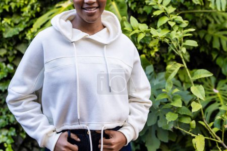 Téléchargez les photos : Midsection de femme afro-américaine heureuse portant sweat à capuche blanc debout dans le jardin. Mode, vêtements décontractés et vêtements de loisir, inchangés. - en image libre de droit