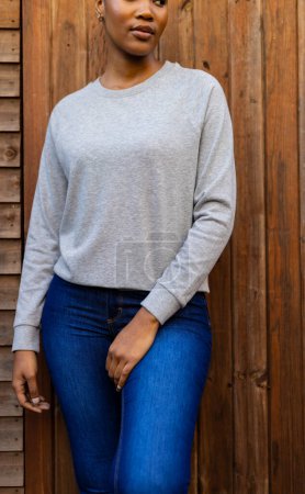 Téléchargez les photos : Midsection de femme afro-américaine portant un sweat-shirt gris contre une clôture en bois. Mode, vêtements décontractés et vêtements de loisir, inchangés. - en image libre de droit
