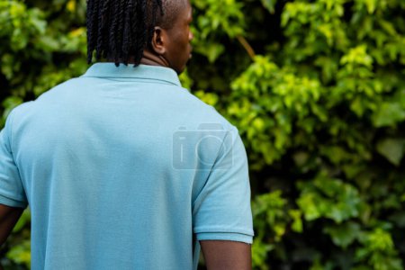 Téléchargez les photos : Vue arrière de l'homme afro-américain avec dreadlocks portant un polo bleu pâle dans le jardin, espace de copie. Mode, vêtements décontractés et vêtements de loisir, inchangés. - en image libre de droit