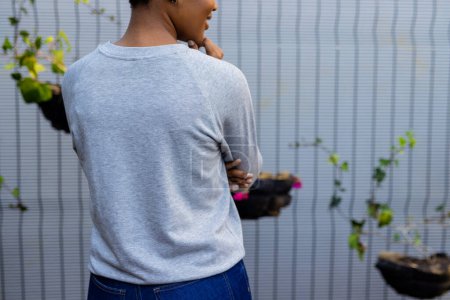 Foto de Vista trasera de sección media de mujer afroamericana en sudadera gris contra valla blanca, espacio para copiar. Moda, ropa casual y ropa de ocio, inalterada. - Imagen libre de derechos