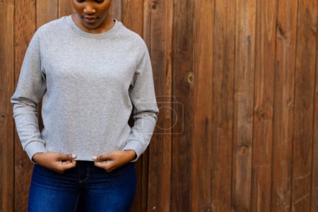 Téléchargez les photos : Midsection de femme afro-américaine portant un sweat-shirt gris contre une clôture en bois, espace de copie. Mode, vêtements décontractés et vêtements de loisir, inchangés. - en image libre de droit