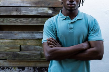 Téléchargez les photos : Milieu de l'homme afro-américain portant un polo bleu pâle contre une clôture en bois, espace de copie. Mode, vêtements décontractés et vêtements de loisir, inchangés. - en image libre de droit