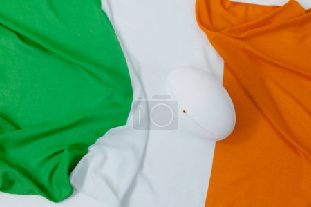 Téléchargez les photos : Ballon de rugby blanc au-dessus du drapeau de l'Irlande avec espace de copie. Rugby, sport, international, compétition et jeux image générée numériquement. - en image libre de droit