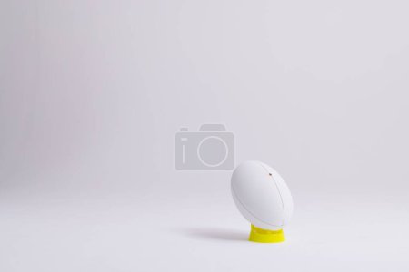 Téléchargez les photos : Balle de rugby blanche sur support jaune avec espace de copie sur fond blanc. Rugby, sport, international, compétition et jeux image générée numériquement. - en image libre de droit
