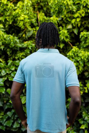 Foto de Vista trasera del hombre afroamericano con rastas que usan polo azul pálido en el jardín. Moda, ropa casual y ropa de ocio, inalterada. - Imagen libre de derechos