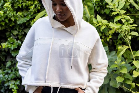 Photo for Happy african american woman wearing white hooded sweatshirt standing in garden. Fashion, casual clothing and leisurewear, unaltered. - Royalty Free Image