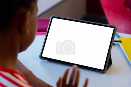 Photo for Rear view of biracial boy having a video call on digital tablet with copy space at school. Distant learning online education concept - Royalty Free Image