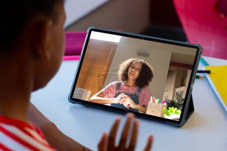 Téléchargez les photos : Vue arrière d'un garçon afro-américain ayant un appel vidéo avec une enseignante sur une tablette à la maison. Concept d'enseignement en ligne à distance - en image libre de droit