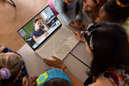 Foto de Maestra asiática y estudiantes diversas que tienen una videollamada con un chico caucásico en la computadora portátil en la escuela. Concepto de educación a distancia en línea - Imagen libre de derechos