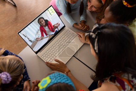 Foto de Maestra asiática y estudiantes diversas que tienen una videollamada en la computadora portátil con una chica en la escuela. Concepto de educación a distancia en línea - Imagen libre de derechos