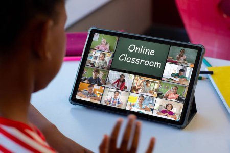 Téléchargez les photos : Africain américain garçon ayant une vidéoconférence avec divers étudiants sur tablette à l'école. Concept d'enseignement en ligne à distance - en image libre de droit