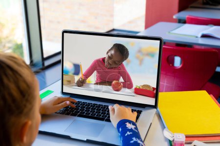 Photo for Rear view of a caucasian girl having a video call with african american girl on laptop at school. Distant learning online education concept - Royalty Free Image