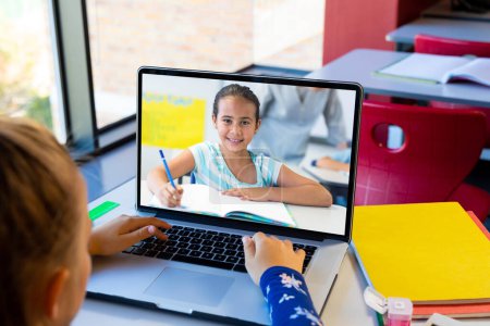 Photo for Rear view of caucasian girl using laptop while having a video call with a biracial girl at school. Distant learning online education concept - Royalty Free Image
