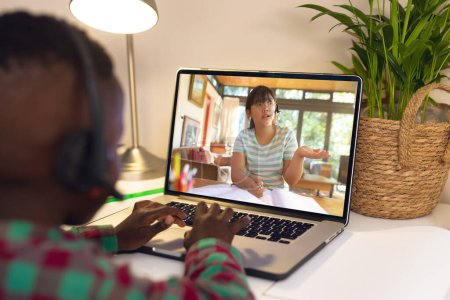 Foto de Vista trasera de un niño afroamericano utilizando el ordenador portátil, mientras que tener una videollamada con chica asiática en casa. Concepto de educación a distancia en línea - Imagen libre de derechos