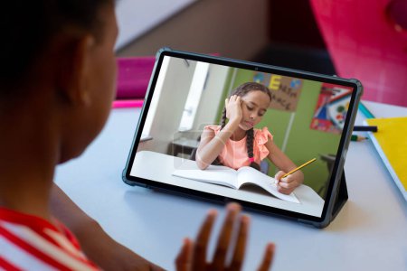 Photo for Rear view of a biracial boy waving while having a video call with biracial girl on tablet at home. Distant learning online education concept - Royalty Free Image