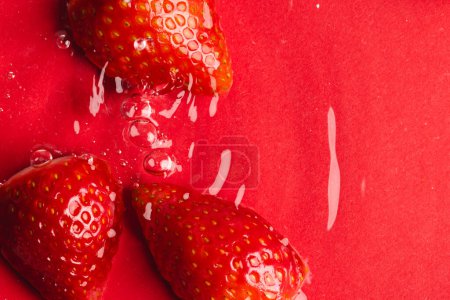 Téléchargez les photos : Gros plan de fraises dans l'eau avec espace de copie sur fond rouge. Fruits, nourriture végétalienne et concept de couleur. - en image libre de droit