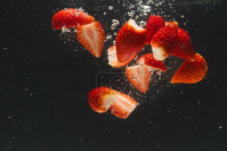 Photo for Close up of strawberries falling into water with copy space on black background. Fruit, vegan food and colour concept. - Royalty Free Image