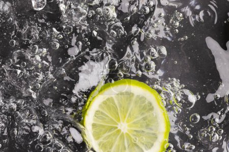 Photo for Close up of lime slice in water with copy space on black background. Fruit, vegan food and colour concept. - Royalty Free Image