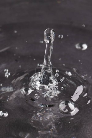 Foto de Primer plano de la gota de agua que cae en el agua con ondas y copiar el espacio en el fondo negro. Concepto de agua, líquido y color. - Imagen libre de derechos