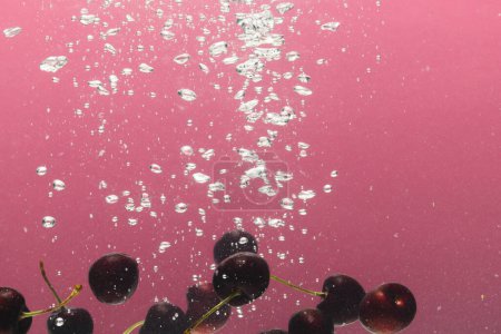 Foto de Primer plano de cerezas que caen en el agua con espacio de copia sobre fondo rosa. Concepto de fruta, comida vegana y color. - Imagen libre de derechos