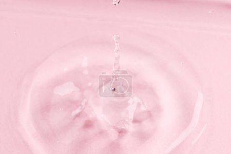 Foto de Primer plano de la gota de agua que cae en el agua con ondas y copiar el espacio en el fondo rosa. Concepto de agua, líquido y color. - Imagen libre de derechos