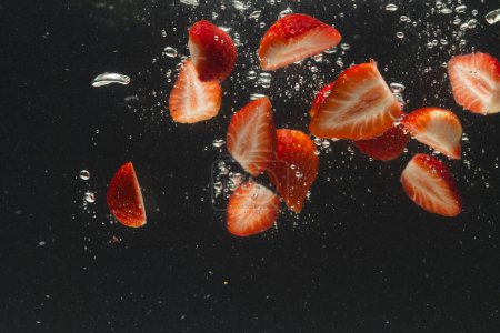 Photo for Close up of strawberries falling into water with copy space on black background. Fruit, vegan food and colour concept. - Royalty Free Image