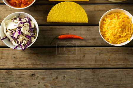Photo for Directly above shot of cheese and cabbage in bowls with tortillas and chili on wooden table. unaltered, taco, ingredients, food, preparation and mexican food concept. - Royalty Free Image