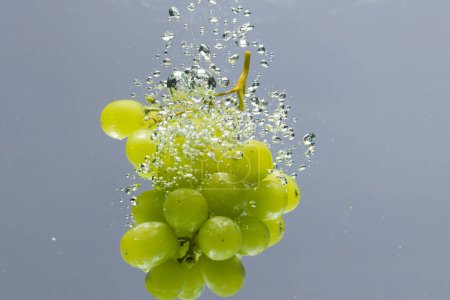 Téléchargez les photos : Gros plan de raisins blancs tombant dans l'eau avec espace de copie sur fond gris. Fruits, nourriture végétalienne et concept de couleur. - en image libre de droit
