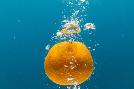 Téléchargez les photos : Gros plan de mandarine tombant dans l'eau avec espace de copie sur fond bleu. Fruits, nourriture végétalienne et concept de couleur. - en image libre de droit