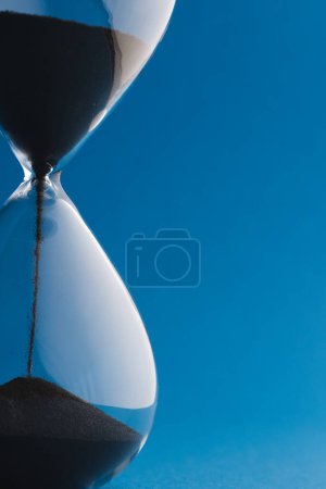 Foto de Primer plano de reloj de arena negra y espacio de copia sobre fondo azul. Tiempo, cronometraje, forma y concepto de color. - Imagen libre de derechos