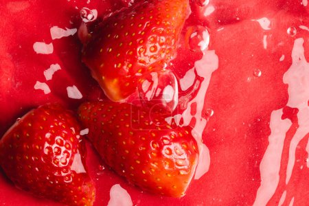 Téléchargez les photos : Gros plan de fraises dans l'eau avec espace de copie sur fond rouge. Fruits, nourriture végétalienne et concept de couleur. - en image libre de droit