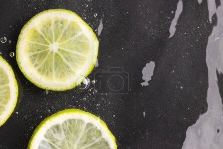 Téléchargez les photos : Gros plan de tranches de citron vert et citron dans l'eau avec espace de copie sur fond noir. Fruits, nourriture végétalienne et concept de couleur. - en image libre de droit