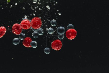 Foto de Primer plano de bayas frescas que caen en el agua con espacio de copia sobre fondo negro. Concepto de fruta, comida vegana y color. - Imagen libre de derechos