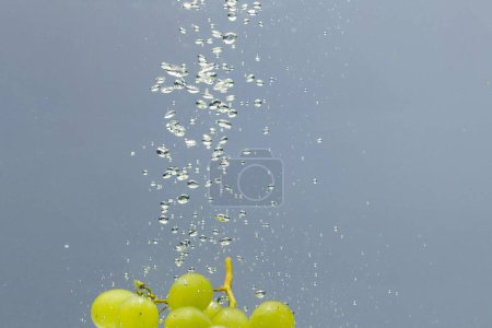 Foto de Primer plano de uvas blancas que caen al agua con espacio de copia sobre fondo gris. Concepto de fruta, comida vegana y color. - Imagen libre de derechos