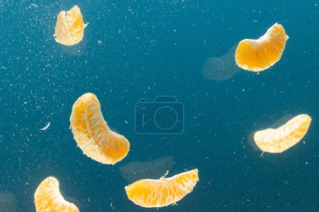 Foto de Primer plano de los segmentos de mandarina que caen al agua con espacio de copia sobre fondo azul. Concepto de fruta, comida vegana y color. - Imagen libre de derechos