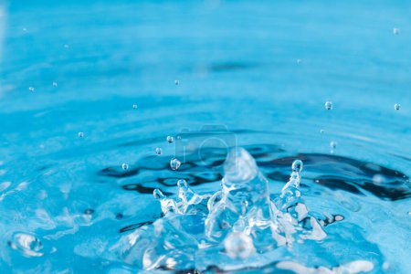 Foto de Primer plano de la gota de agua que cae en el agua con ondas y copiar el espacio en el fondo azul. Concepto de agua, líquido y color. - Imagen libre de derechos