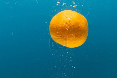 Photo for Close up of tangerine falling into water with copy space on blue background. Fruit, vegan food and colour concept. - Royalty Free Image