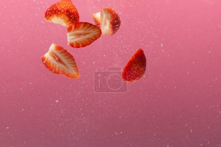 Téléchargez les photos : Gros plan de fraises tombant dans l'eau avec espace de copie sur fond rose. Fruits, nourriture végétalienne et concept de couleur. - en image libre de droit