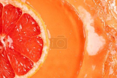 Photo for Close up of red grapefruit slice in water with copy space on orange background. Fruit, vegan food and colour concept. - Royalty Free Image