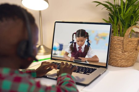 Téléchargez les photos : Vue arrière d'un garçon afro-américain utilisant un ordinateur portable tout en ayant un appel vidéo avec une fille biraciale. Concept d'enseignement en ligne à distance - en image libre de droit