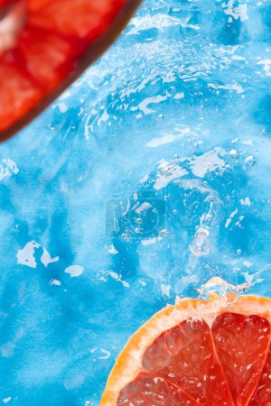 Photo for Close up of red grapefruit slices in water with copy space on blue background. Fruit, vegan food and colour concept. - Royalty Free Image