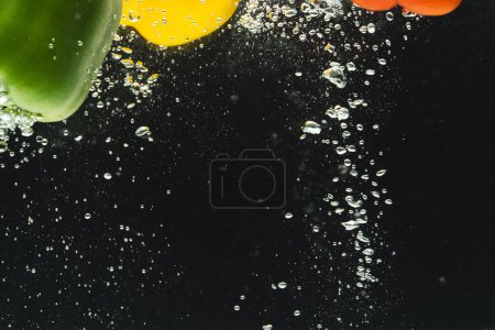 Photo for Close up of peppers falling into water with copy space on black background. Vegetables, vegan food and colour concept. - Royalty Free Image