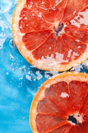 Foto de Primer plano de rodajas de pomelo rojo en agua con espacio para copiar sobre fondo azul. Concepto de fruta, comida vegana y color. - Imagen libre de derechos