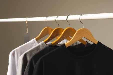 Foto de Cuatro camisetas en perchas colgando de riel de ropa y espacio de copia sobre fondo gris. Moda, ropa, color y concepto de tela. - Imagen libre de derechos