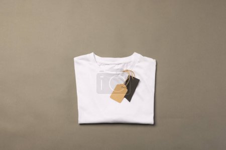 Foto de Camiseta blanca plegada con etiquetas con espacio de copia sobre fondo marrón. Moda, ropa, color y concepto de tela. - Imagen libre de derechos