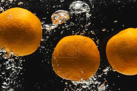 Foto de Primer plano de naranjas que caen al agua con espacio de copia sobre fondo negro. Concepto de frutas, alimentos, frescura y color. - Imagen libre de derechos