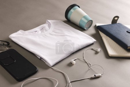 Téléchargez les photos : Pose plate de t-shirt blanc, smartphone, écouteurs et ordinateurs portables avec espace de copie sur fond gris. Mode, vêtements, concept de couleur et de tissu. - en image libre de droit