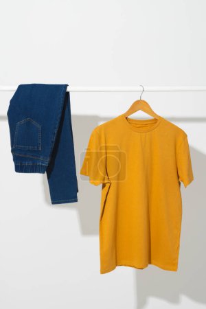 Photo for Yellow t shirt and denim trousers on clothes rail with copy space on white background. Fashion, clothes, colour and fabric concept. - Royalty Free Image