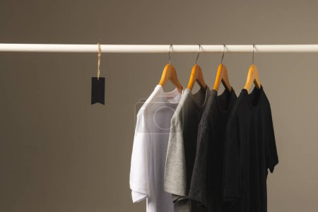 Photo for Four t shirts on hangers hanging from clothes rail and copy space on grey background. Fashion, clothes, colour and fabric concept. - Royalty Free Image